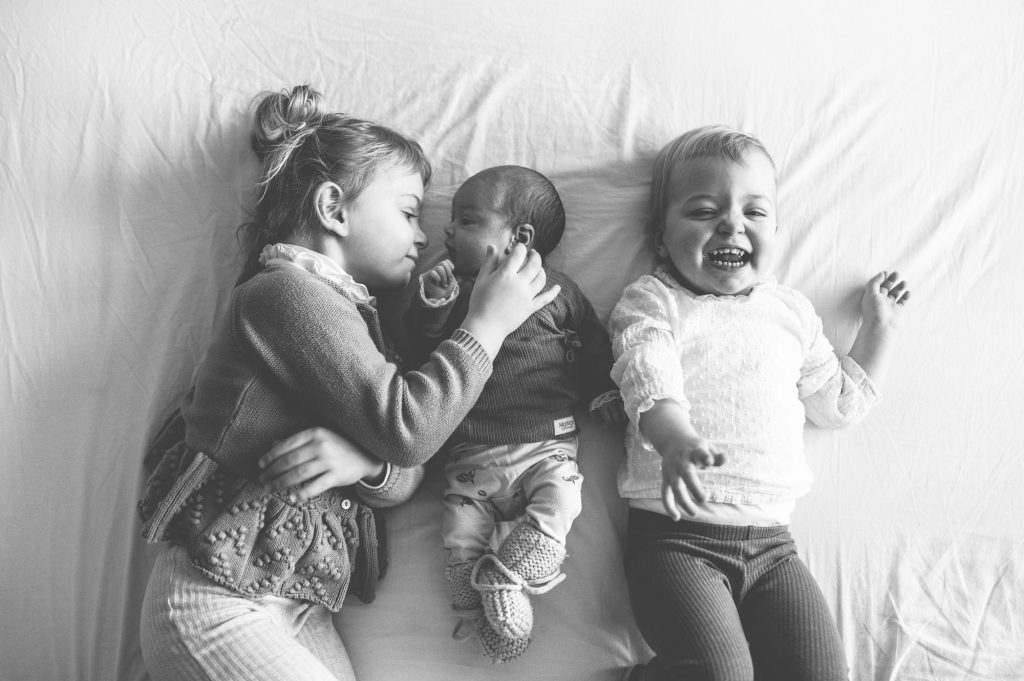Grote broer en zus knuffelen baby op bed.